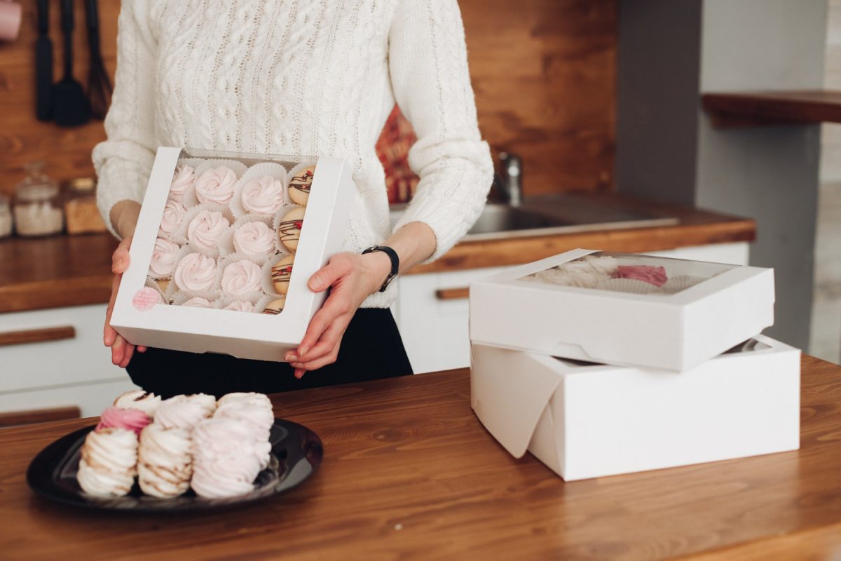 Une femme présente un emballage personnalisé pour pâtisserie à Lyon contenant des meringues et macarons.
